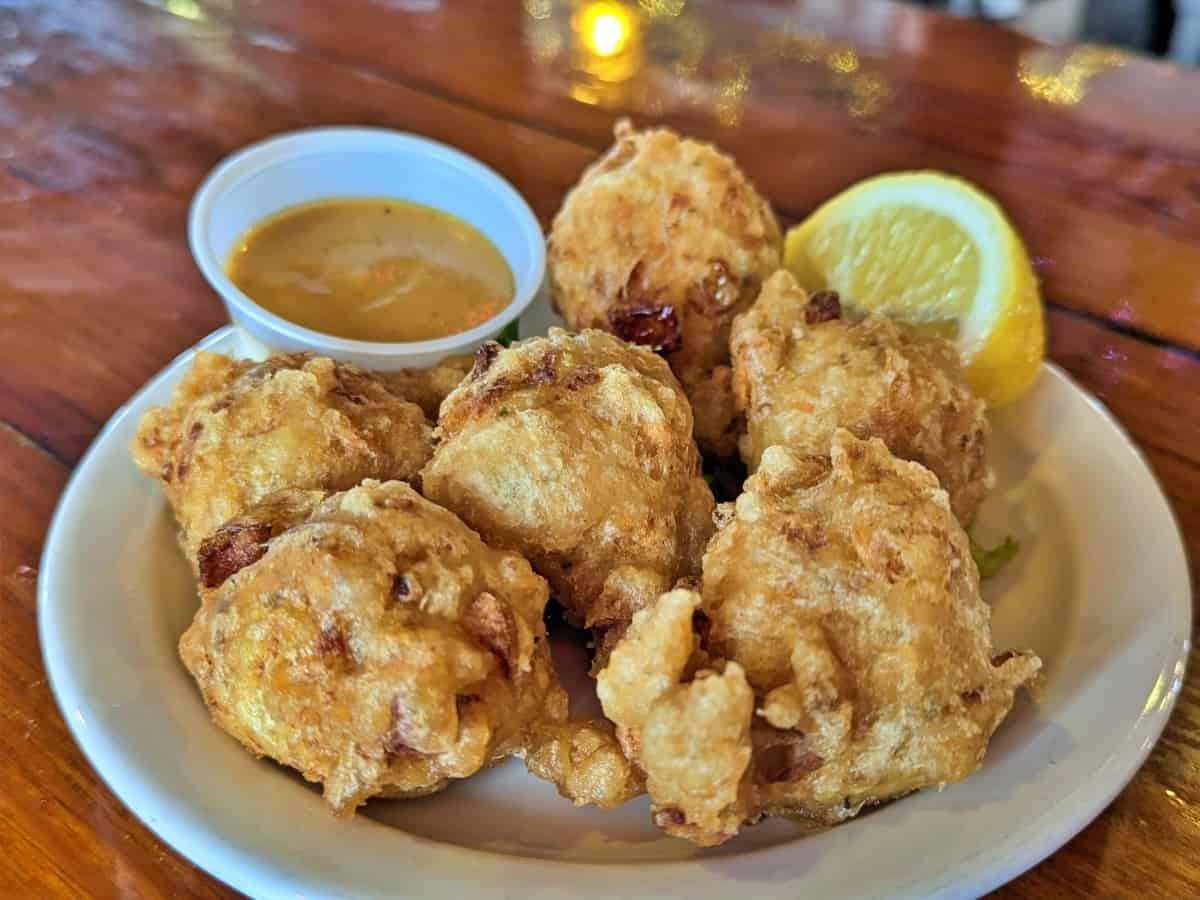 A plate of conch fritters with dipping sauce and lemon wedge