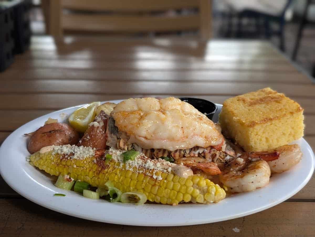 Lobster tail, grilled shrimp, corn, red potatoes and cornbread on a white plate at the Key West Lobsterfest Lobster Boil